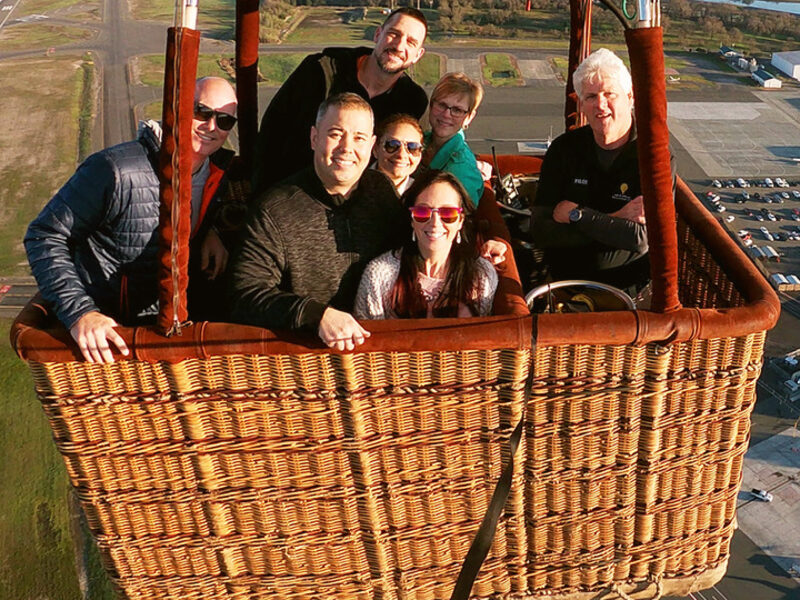Six guests and their pilot smiling from the basket high above the valley