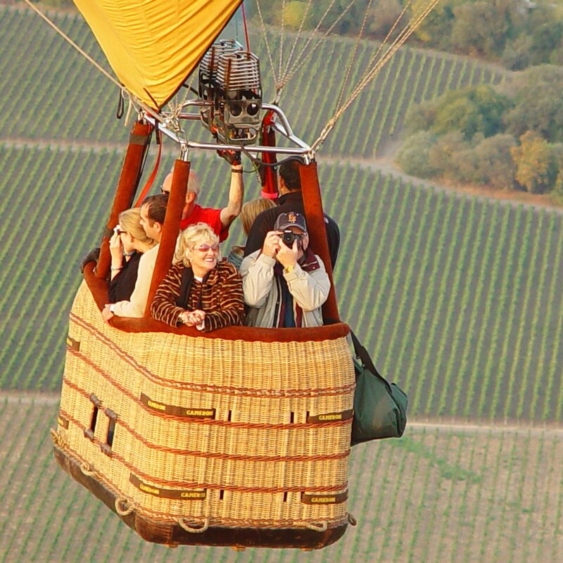 Guests waving from the basket above golden vineyards